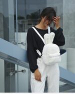 White plushie rabbit backpack worn by a woman, featuring furry rabbit ears.