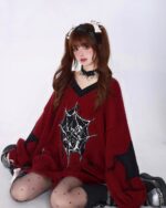 Model wearing a red loose gothic sweater with a spiderweb design and black accents.