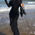 Black gothic aesthetic dress worn on a beach; long sleeves and a high slit.