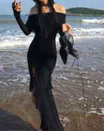 Black gothic aesthetic dress worn on a beach; long sleeves and a high slit.