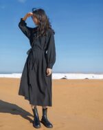 Black korean style dress with long sleeves, belted waist, and boots on a sandy beach.
