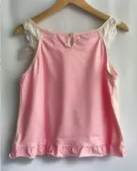 Pink mezzo piano tank top, featuring white polka dots and lace accents, hanging on a hanger.