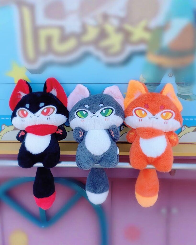 Three kawaii kitsune fox plushies in black, gray, and orange. Soft, cuddly toys.