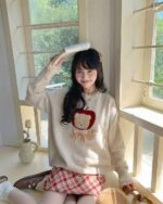 A beige cottagecore bear sweater with an apple motif, worn by a woman.