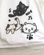 White t-shirt with a playful design featuring three neko cat illustrations and musical notes. A neko cat t-shirt.