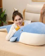 Blue and white kawaii whale plushie lying on a bed with a person.