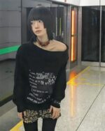 Model wearing a black grunge aesthetic sweater with a distressed print, standing in a subway station.