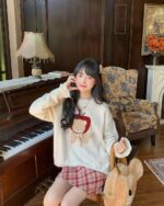 A woman wearing a cream-colored cottagecore bear sweater with a red apple graphic.