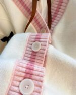 Close-up of a kawaii bow sweater with multiple buttons and a pink plaid pattern.