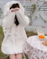 Fluffy bunny ears coat featuring a hooded design and pom-poms. Soft, plush material.