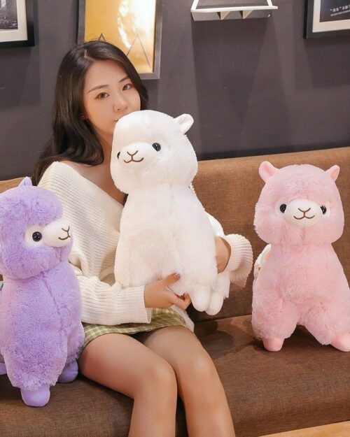 Three colorful alpaca plush toys in lavender, white, and pink, displayed on a sofa.