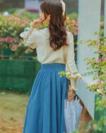 Woman wearing a cottagecore dress with a blue skirt and cream blouse, holding an umbrella.