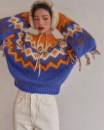 Blue and orange kawaii winter sweater with tassels, styled with earmuffs and white pants.
