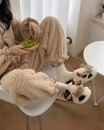 A pair of brown cow slippers with a cute design, displayed on a wooden floor.