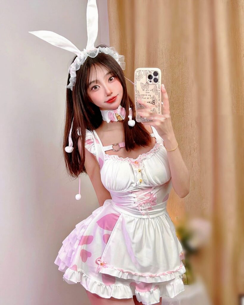 A woman wearing a bunny girl maid costume, featuring pink and white frills, ears, and a bib.