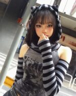 A person wearing a black and gray striped off-shoulder hoodie and a cat ear headband.