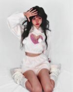 A person wearing a kawaii fluffy pajamas set, featuring a white cropped hoodie with a heart-shaped patch and matching shorts.