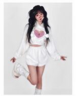 Model wearing a white kawaii fluffy pajamas set, featuring a hooded sweatshirt and shorts with heart accents.