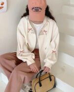 Close-up of a romantic zipper hoodie featuring ‘LONG ISLAND’ embroidery and bows.