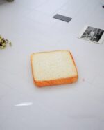 A plush toast cat bed displayed on a white floor.