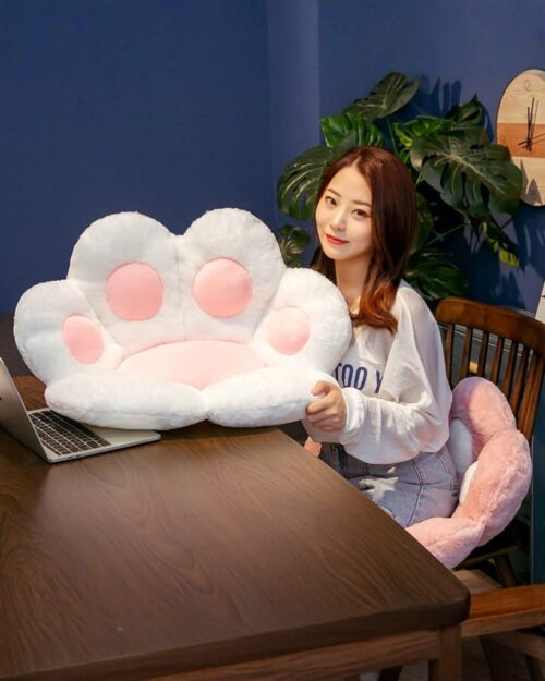 Kawaii neko pillow featuring a fluffy white paw print design with pink details, resting on a wooden table.