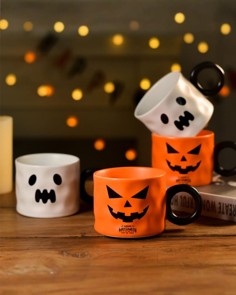 Set of Halloween pumpkin cups with pumpkin and ghost designs, ceramic mugs.
