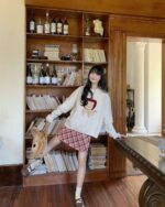 Woman wearing a cottagecore bear sweater, grey knit with bear design, layered with a plaid skirt.