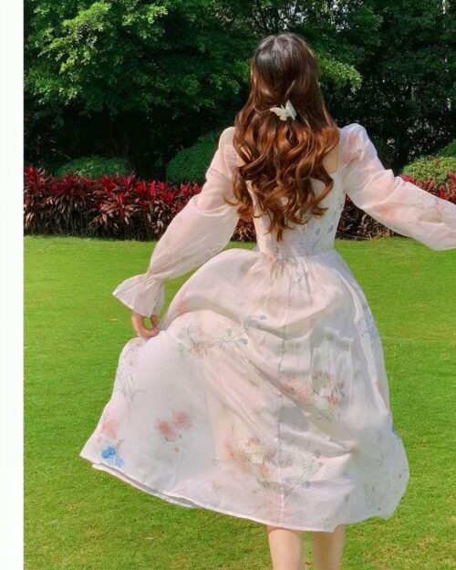 Woman wearing a pale pink french floral dress in a grassy outdoor setting.