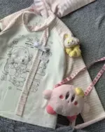 Nyanko Pink T-Shirt with plush toys and accessories on a pink and white striped background.