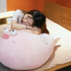 A pink pufferfish plush toy, resting on a bed with a person.