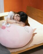 A pink pufferfish plush toy, resting on a bed with a person.