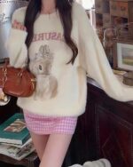 Cream-colored Treasure Bag bunny aesthetic sweater worn with a pink skirt and handbag.