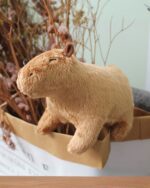 A plush brown capybara toy sits among dried flowers and foliage.