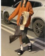 Model wearing a Korean aesthetic sweater, loose-fit orange pullover with a gray skirt and sandals.