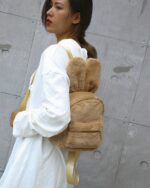 Brown plushie rabbit backpack worn by a woman, featuring floppy ears and a zipper closure.