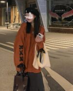 Woman wearing a Korean aesthetic sweater, loose-fit, orange color, with accessories.