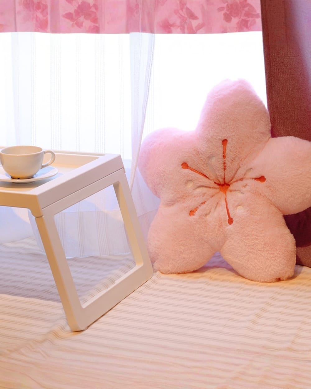 Pink sakura flower pillow on a white table, with a cup and window light.