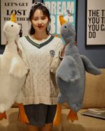 Two big goose plush toys displayed with a person. One is white, the other is gray.