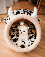 A cozy kawaii cat bed with cow print, featuring a small dog resting inside.