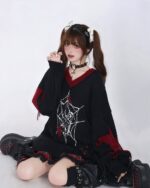Woman wearing a black loose gothic sweater with spiderweb and heart embroidery, paired with combat boots.
