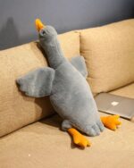 Grey big goose plush resting on a sofa with a laptop.