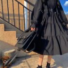 Black gothic lolita dress with ruffles and a belt, outdoor setting.