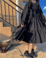 Black gothic lolita dress with ruffles and a belt, outdoor setting.