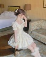 Cream vintage aesthetic dress with square collar, seated in a hotel room.