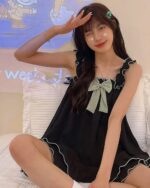 Model wearing black soft girl pajamas with a pale green bow. The soft girl pajamas feature ruffled details.