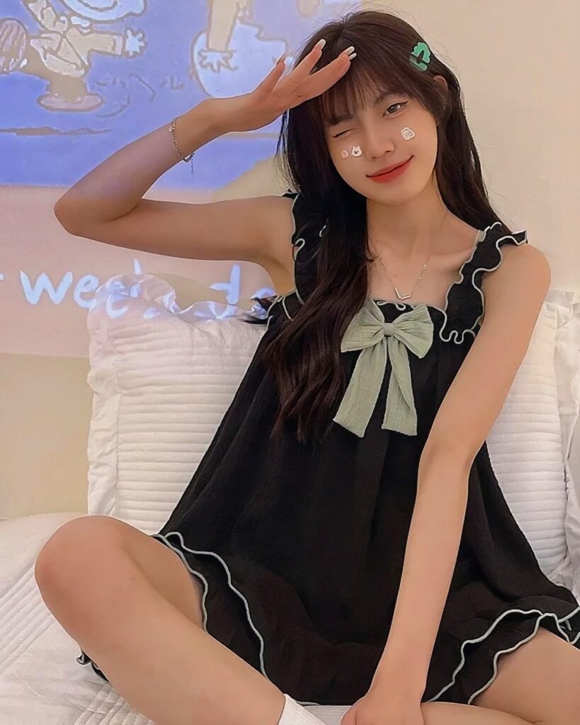 Model wearing black soft girl pajamas with a pale green bow. The soft girl pajamas feature ruffled details.
