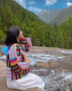 Woman wearing a vibrant retro knitted cardigan amidst a mountain landscape.