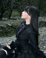 Woman wearing a black laced gothic lolita dress in a natural setting.