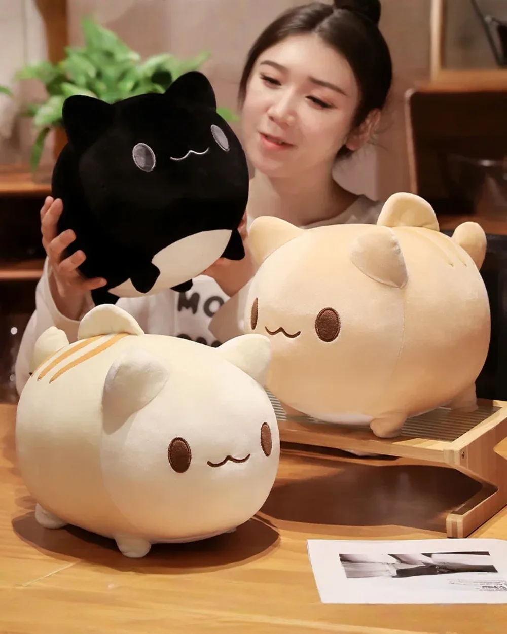 Two Round Neko Plushies, a black and a white, displayed on a wooden table.