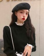 Woman wearing a black french aesthetic top with a ruffled collar and pearl necklace.